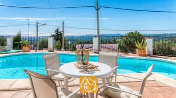 Essbereich im Freien am Pool der Villa Sofia mit einem weißen Resintisch, vier passenden Stühlen mit Kissen und einer Korblaterne als Mittelstück mit Blick auf die fernen Hügel.