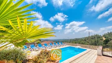 Privater Pool mit blauen Liegen und einem Palmwedel im Vordergrund an der Villa Santa Maria unter einem blauen Himmel mit vereinzelten Wolken.