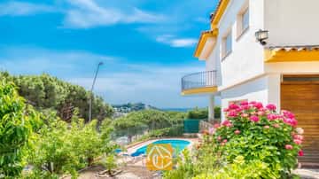 Außenansicht der Villa Valentina mit Swimmingpool, Sonnenliegen und rosa blühenden Büschen vor einer weiß-gelben Fassade.