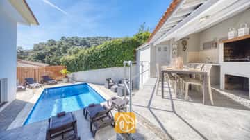 Die Villa Rosa von außen, mit einem blauen Swimmingpool, Sonnenliegen und einer überdachten Essterrasse im Freien inklusive integriertem Grill.