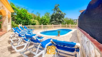 Privater Außenpool der Villa Sarai, umgeben von blauen Sonnenliegen, steinernen Terrassenplatten und grünen Bäumen unter einem strahlend blauen Himmel