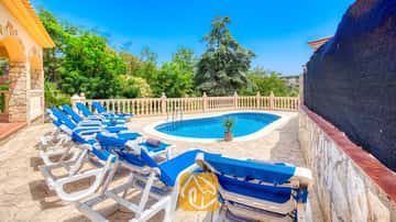 Privater Außenpool der Villa Sarai, umgeben von blauen Sonnenliegen, steinernen Terrassenplatten und grünen Bäumen unter einem strahlend blauen Himmel