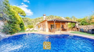 Privater Swimmingpool mit Steinwasserfall an der Villa Alba, mit einem Ziegelstein-Außenbereich, einer überdachten Terrasse und Sonnenliegen auf Kunstrasen unter blauem Himmel.