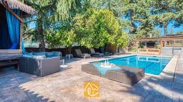 Privater Außenpool der Villa Can Bernardi, ausgestattet mit einem grauen Rattansofa, Sonnenliegen und einem von Bäumen umgebenen Grillbereich im Freien.