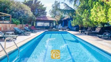 Rechteckiger Swimmingpool der Villa Can Bernardi, umgeben von grünen Sonnenliegen, Bäumen und einem ziegelgedeckten Außenpavillon.