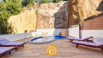 Der private Pool der Villa Blanca mit blauen Mosaikfliesen liegt auf einer gefliesten Terrasse, die von einer hohen Felswand eingerahmt wird, und lädt mit Holzliegen und violetten Kissen zum Entspannen ein.