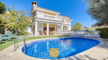 Ein privater Pool mit klarem, blauem Wasser und Metallhandläufen vor der zweistöckigen Fassade der Villa Baileys, die weiße Säulen, Balkone und ein Ziegeldach vor einem blauen Himmel zeigt.