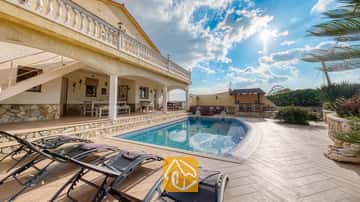 Privater Pool mit Sonnenliegen auf der gefliesten Terrasse der Villa Madonna in Spanien, mit einer überdachten Terrasse und Natursteinmauern unter sonnigem Himmel