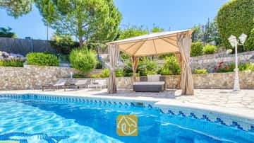 Privater Pool der Villa Lorena mit blau gefliesten Rändern, einem beige Pavillon aus Stoff über den Sitzmöbeln im Freien, Natursteinmauern und umgebendem Grün.