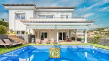 Außenansicht der Villa Madison mit einem blau gefliesten Swimmingpool, Sonnenliegen und einer überdachten Terrasse mit weißen Säulen vor einem klaren blauen Himmel