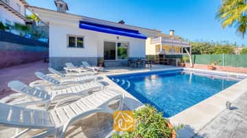 Ein privater Pool mit weißen Sonnenliegen säumt die geflisterte Terrasse der Villa Zarita unter strahlend blauem Himmel.