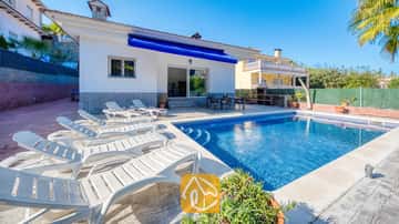 Ein privater Pool mit weißen Sonnenliegen säumt die geflisterte Terrasse der Villa Zarita unter strahlend blauem Himmel.