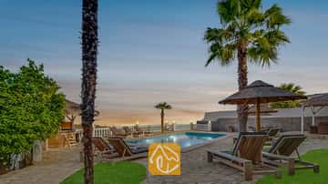 Der private Außenpool der Villa Tropicana, umgeben von Holzliegen, Palmen und Strohschirmen unter einem abendlichen Himmel.