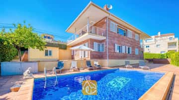 Außenansicht der Villa Beyonce mit einem rechteckigen, blau gefliesten Swimmingpool, Sonnenliegen und einem zweistöckigen Backsteingebäude unter einem blauen, wolkenlosen Himmel