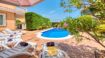Das private Außenpool der Villa Primavera ist von einer gefliesten Terrasse, weißen Sonnenliegen mit gerollten dunklen Handtüchern und blühenden rosafarbenen Oleanderzweigen umgeben.