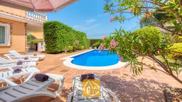 Das private Außenpool der Villa Primavera ist von einer gefliesten Terrasse, weißen Sonnenliegen mit gerollten dunklen Handtüchern und blühenden rosafarbenen Oleanderzweigen umgeben.