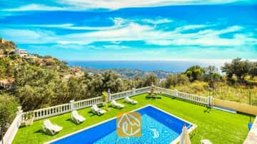 Ein privater Pool und eine grüne Rasenfläche in der Villa Sunrise, ausgestattet mit weißen Sonnenliegen und einer weißen Terrassenbalustrade, die unter einem blauen Himmel den Blick auf das Meer und die Hügel freigibt.