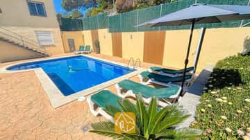 Der private Außenpool der Villa Holiday ist von grünen Sonnenliegen, einem dunklen Sonnenschirm und einem steinernen Terrassenboden umgeben.