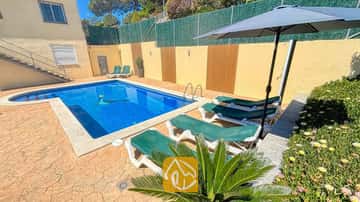 Der private Außenpool der Villa Holiday ist von grünen Sonnenliegen, einem dunklen Sonnenschirm und einem steinernen Terrassenboden umgeben.