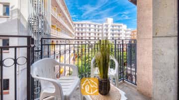 Balkon des Apartment Gaudi mit zwei weißen Plastikstühlen, einem kleinen Tisch mit einer Topfpflanze und einem Metallgeländer mit Blick auf die benachbarten weißen Gebäude.