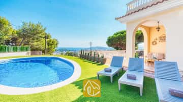 Privater Pool und blaue Holzsonnenliegen auf Kunstrasen an der Villa Ibiza mit Blick auf das weite Meer und die Bäume.