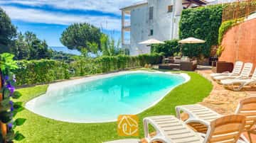 Privater Pool mit Sonnenliegen und Sitzgelegenheiten im Freien in der Villa Sunny Beach in Spanien, umgeben von einem grünen Rasen, ergänzt durch weiße Sonnenschirme und mit Blick auf das Meer im Hintergrund.