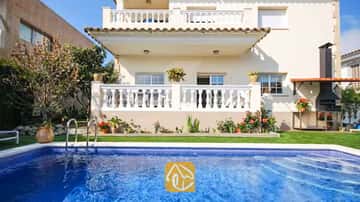 Privater Pool mit azurblauem Wasser vor der Außenfassade der Villa Mercedes Fenals mit weiß balustradierten Balkonen, Rasenfläche und gemauertem Außengrill.