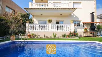 Privater Pool mit azurblauem Wasser vor der Außenfassade der Villa Mercedes Fenals mit weiß balustradierten Balkonen, Rasenfläche und gemauertem Außengrill.
