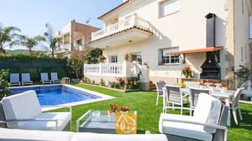 Außenansicht der Villa Mercedes Fenals mit Swimmingpool, Rasenfläche, weißen Gartenmöbeln und einem gemauerten Außen-Grill vor der cremefarbenen Fassade.